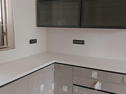 : A clean and minimalist kitchen corner in Bangalore, showcasing white countertops and cabinets with a window providing natural light.