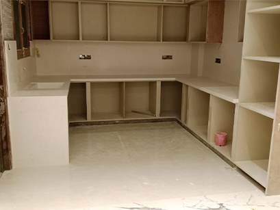  A kitchen in Bangalore under installation, featuring wooden cabinets and shelves with space for countertops yet to be installed.