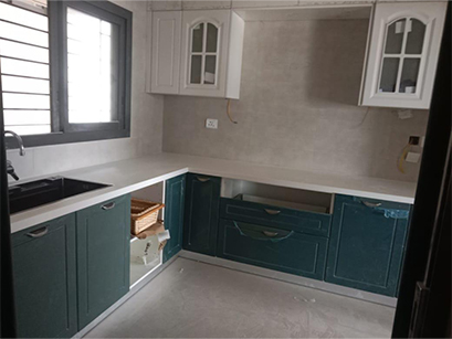  A kitchen in Bangalore with white countertops, green cabinets, glass-paneled upper cabinets, and a window for a modern and airy look.