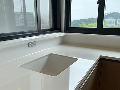 A functional kitchen design in Bangalore featuring a white countertop with a large sink, complemented by a window above.